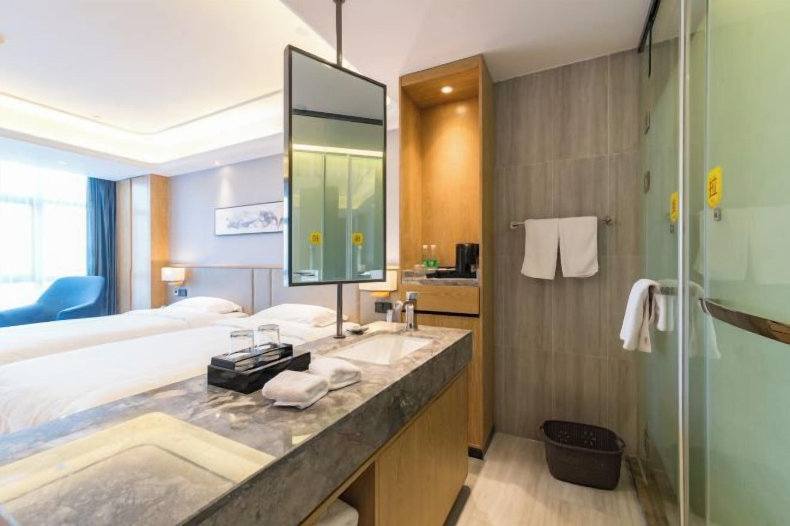 Una habitación de hotel con cama, baño con lavamanos, espejo y ducha.