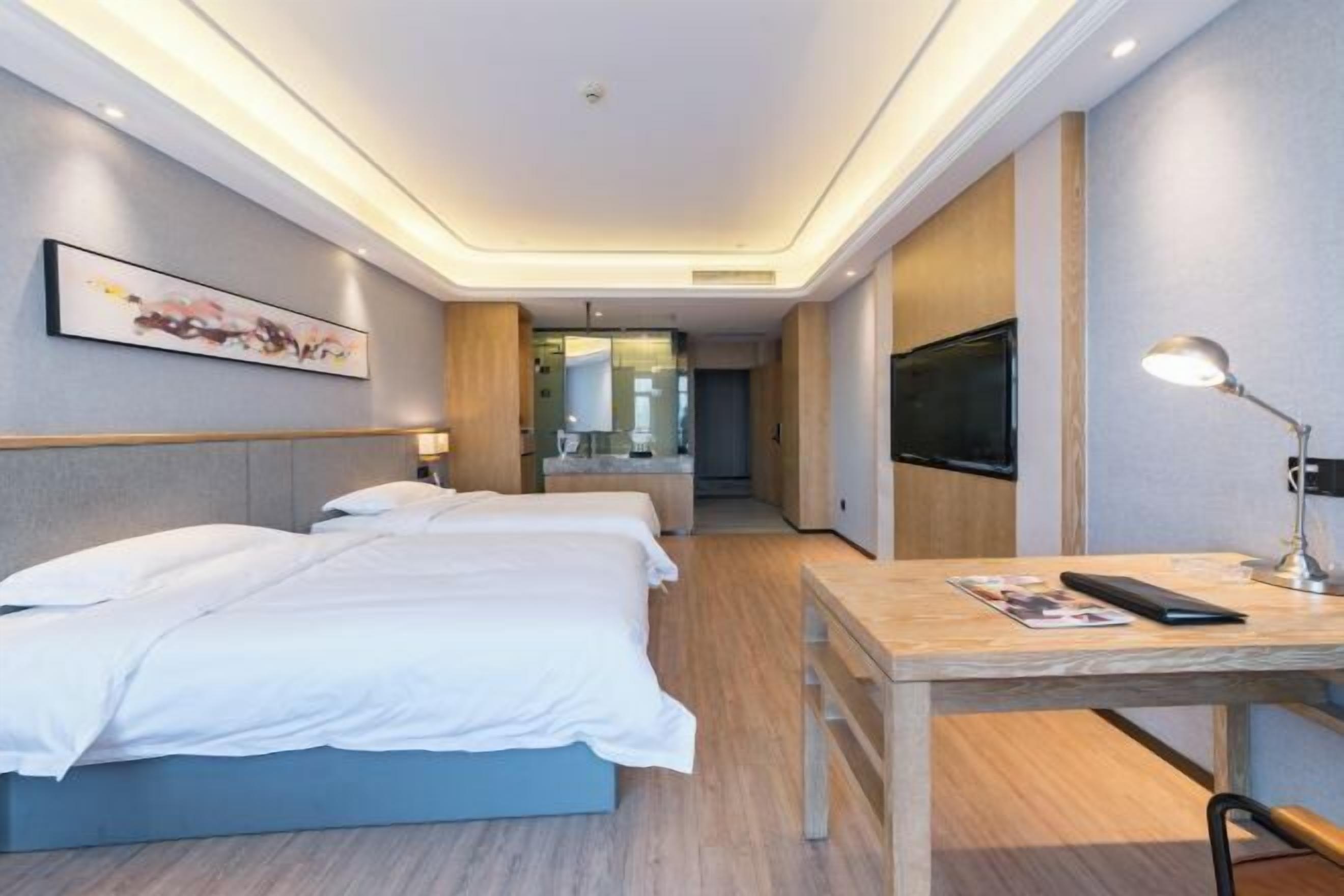 Habitación de hotel moderna con una cama grande, un escritorio, un televisor y un baño visible a través de una puerta de cristal.