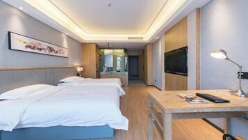Habitación de hotel moderna con una cama grande, un escritorio, un televisor y un baño visible a través de una puerta de cristal.