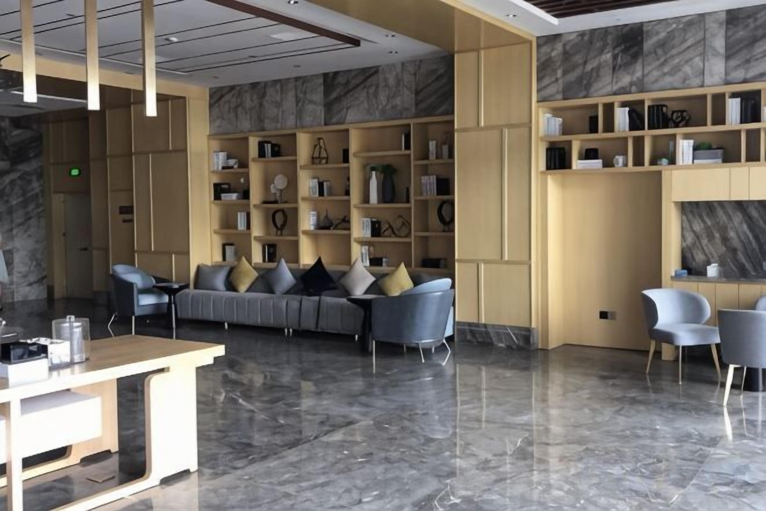 A modern lobby with a sofa, chairs, marble flooring, and shelves with books and decorative items.