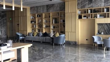 A modern lobby with a sofa, chairs, marble flooring, and shelves with books and decorative items.