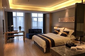 A modern hotel room with a large bed, bedside tables, a desk, and a seating area.