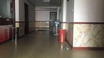 A hotel corridor with a trash bin, a fan, and a door in the background.