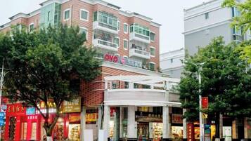 A multi-story building with a prominent OYO hotel sign, surrounded by various shops and a tree-lined street.