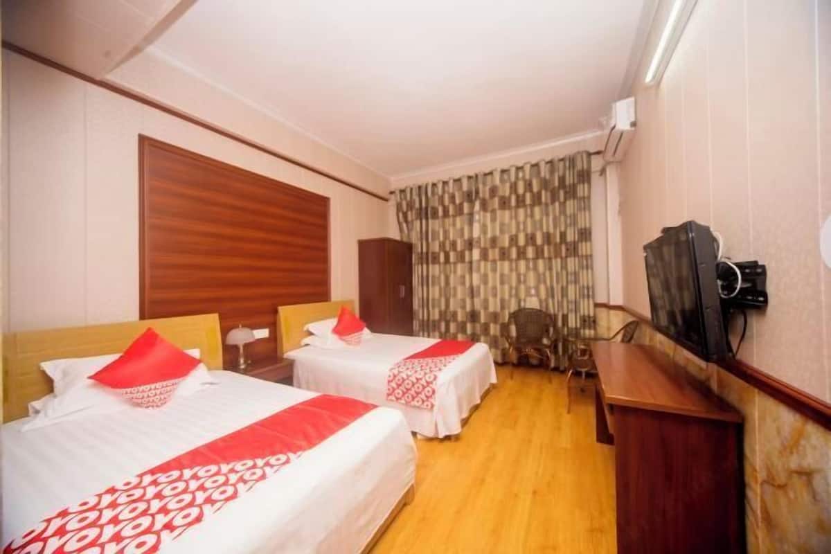A hotel room with two beds, a wooden headboard, a television, and a desk.