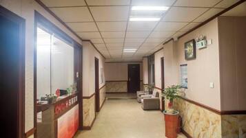 A hotel corridor with a reception desk, seating area, and a clock on the wall.