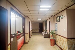 A hotel corridor with a reception desk, seating area, and a clock on the wall. - Changtai Dongyuan Hotel (Zhangzhou)