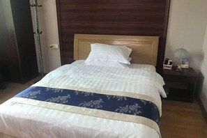 A neatly made bed with a wooden headboard, a bedside table with a lamp, and a wall-mounted radiator. - Changtai Dongyuan Hotel (Zhangzhou)