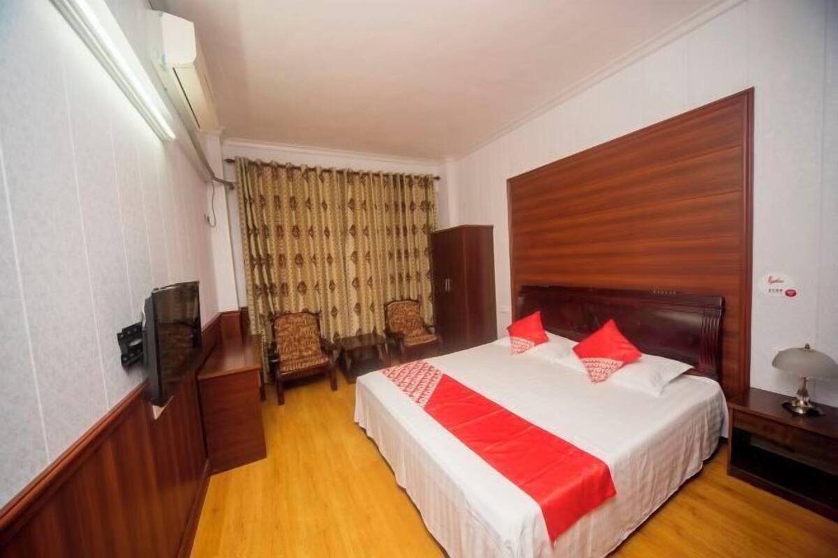 A hotel room with a large bed, a television, a wardrobe, and a desk with a lamp.