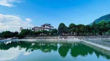 A building with a reflection in a calm body of water, surrounded by trees and a clear sky.