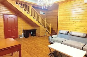 A wooden interior with a staircase, a sofa, a table, and a door.