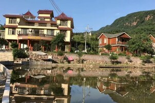 Un edificio tradicional reflejado en aguas tranquilas, rodeado de follaje y colinas.