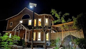 Ein zweistöckiges Holzhaus mit einer Veranda, einer Straßenlaterne und einem reetgedeckten Gebäude im Hintergrund.