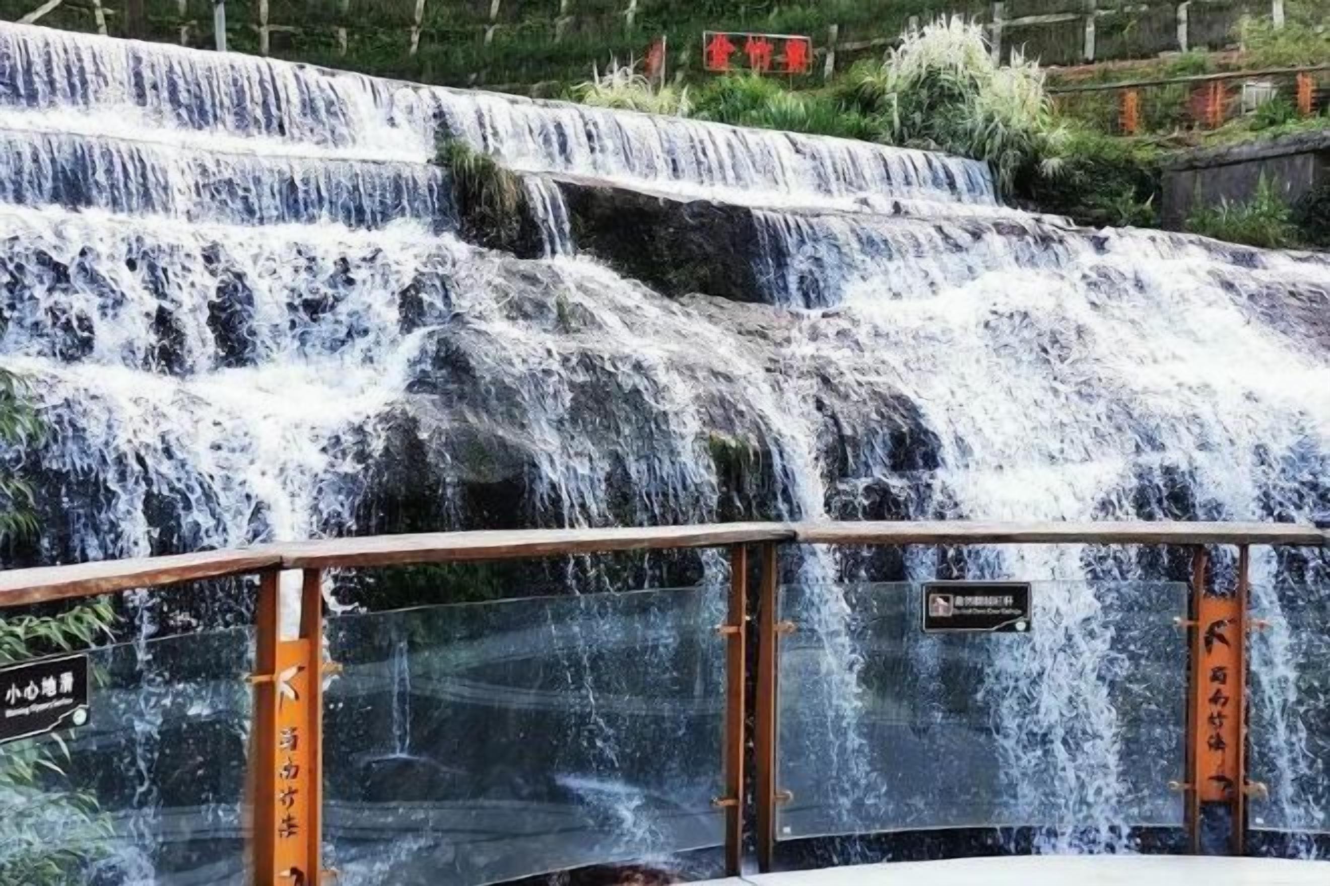 Una cascada con varios niveles y una barandilla de cristal en primer plano.