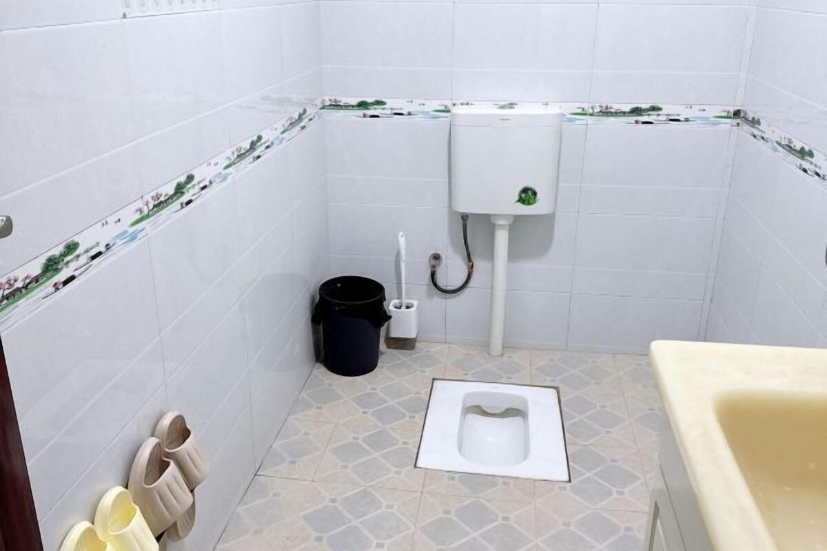 A small bathroom with a toilet, a sink, and a pair of slippers against the wall.