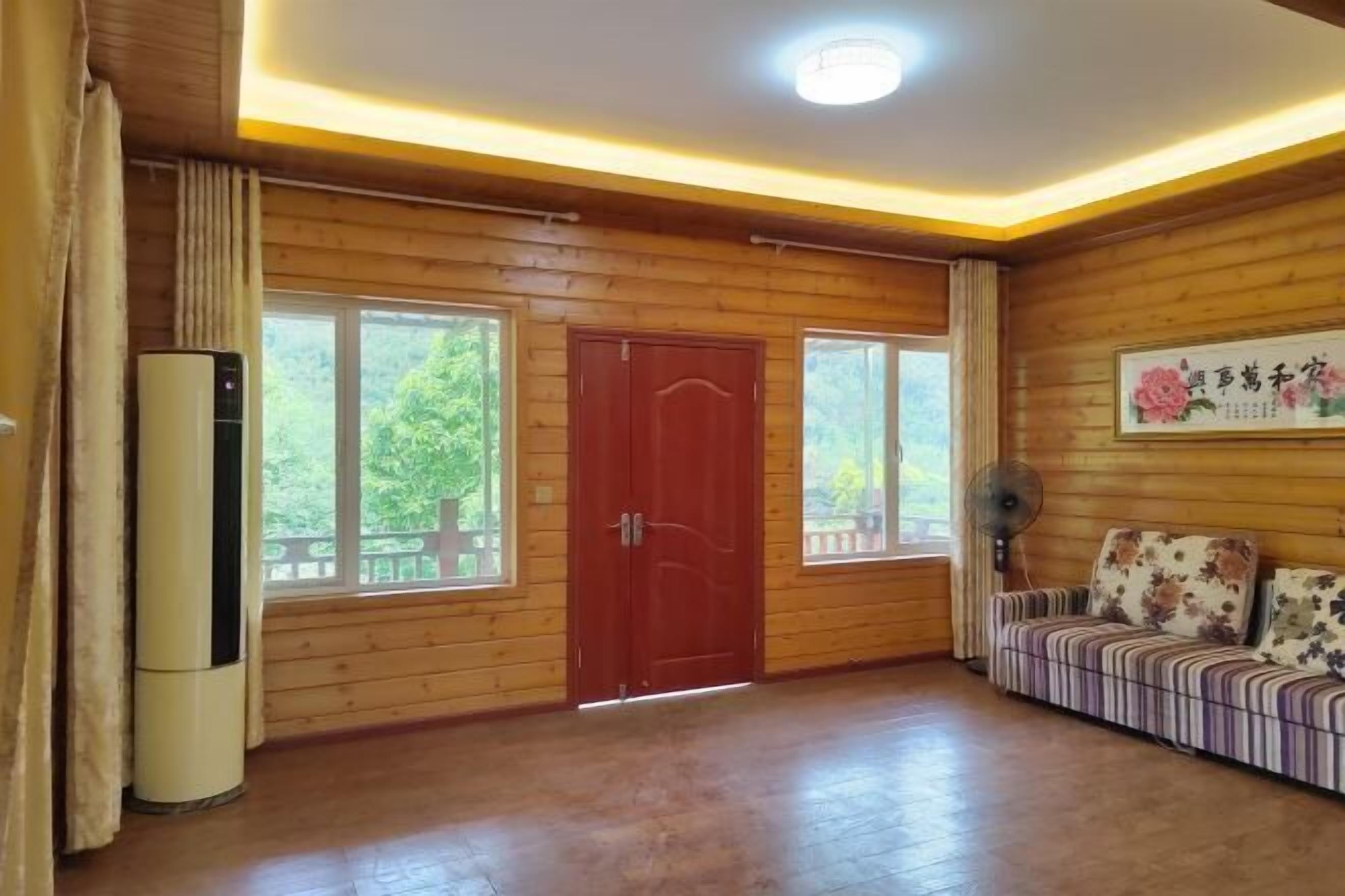 A wooden-paneled room with a red door, a sofa, a fan, and an air conditioning unit.