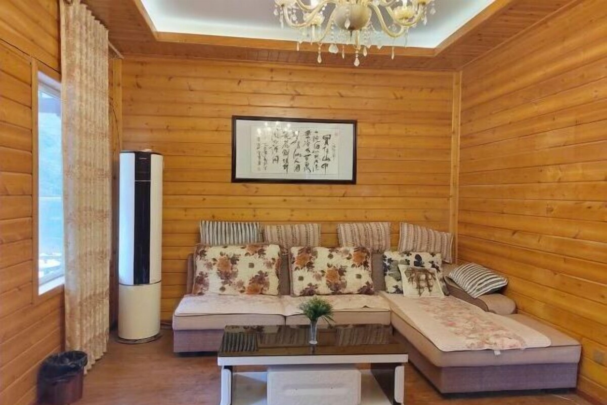 A cozy room with wooden walls, a sofa with floral cushions, a small table, and a framed artwork on the wall.