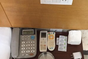 Un bureau avec un téléphone, une télécommande, une boîte de mouchoirs, un verre et un adaptateur secteur.
