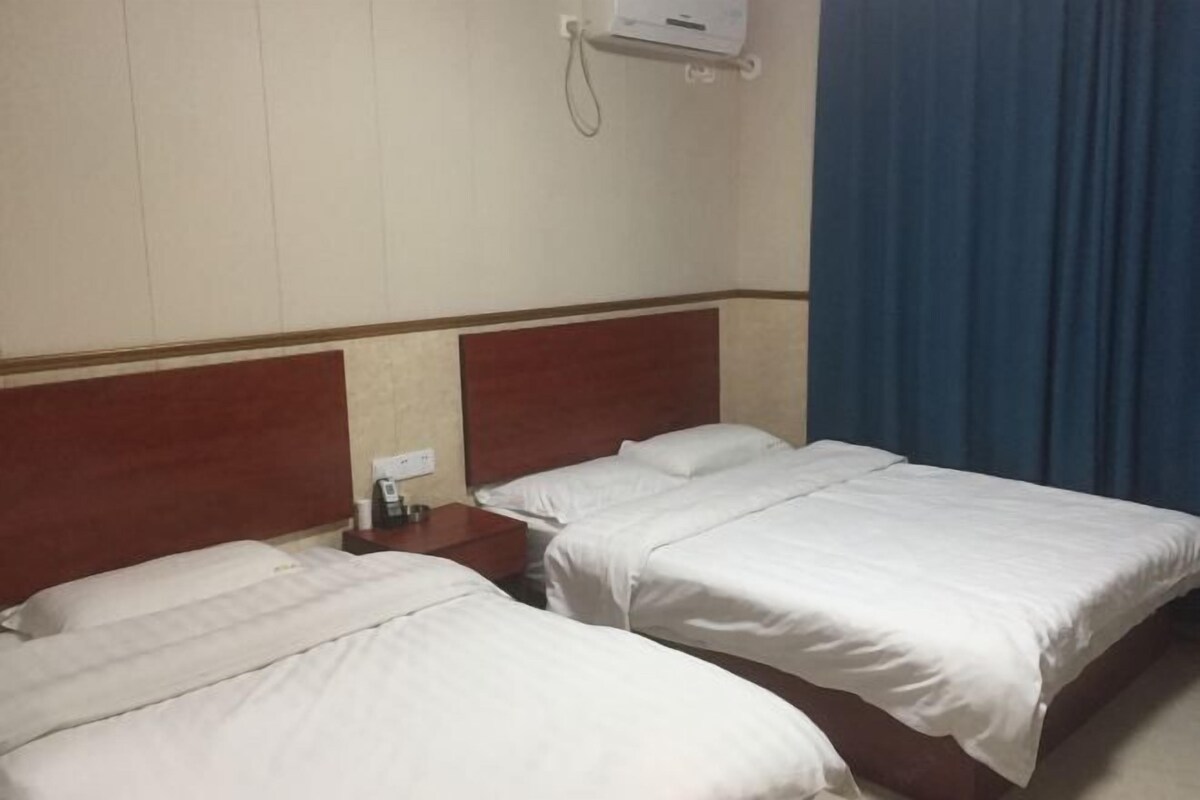 Une chambre d’hôtel avec deux lits simples, une tête de lit en bois, une table de chevet avec une lampe et un téléphone.