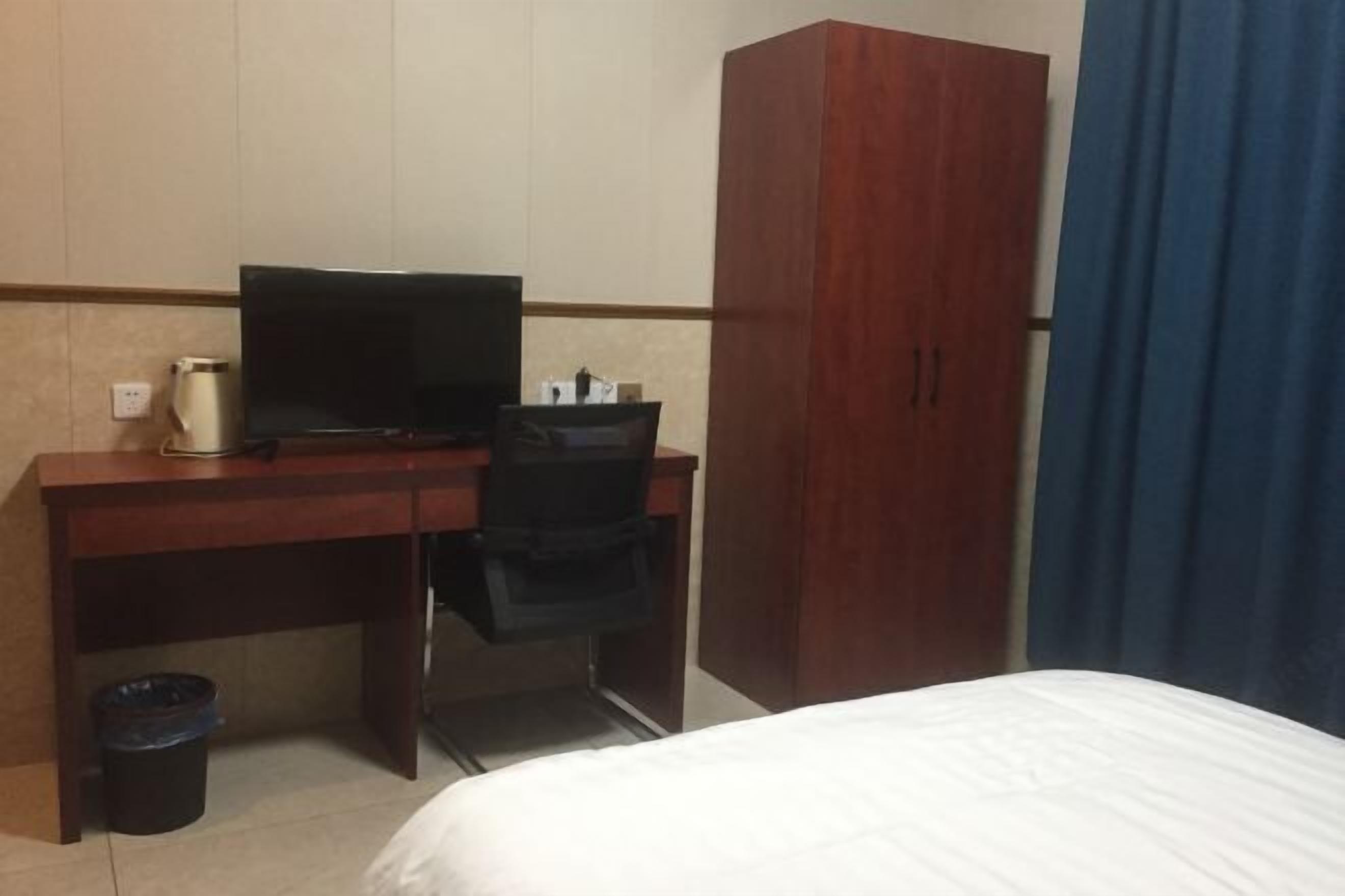Une chambre d’hôtel comprenant un lit, un bureau avec une télévision, une armoire et une poubelle.