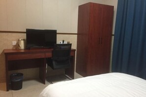 Une chambre d’hôtel comprenant un lit, un bureau avec une télévision, une armoire et une poubelle.
