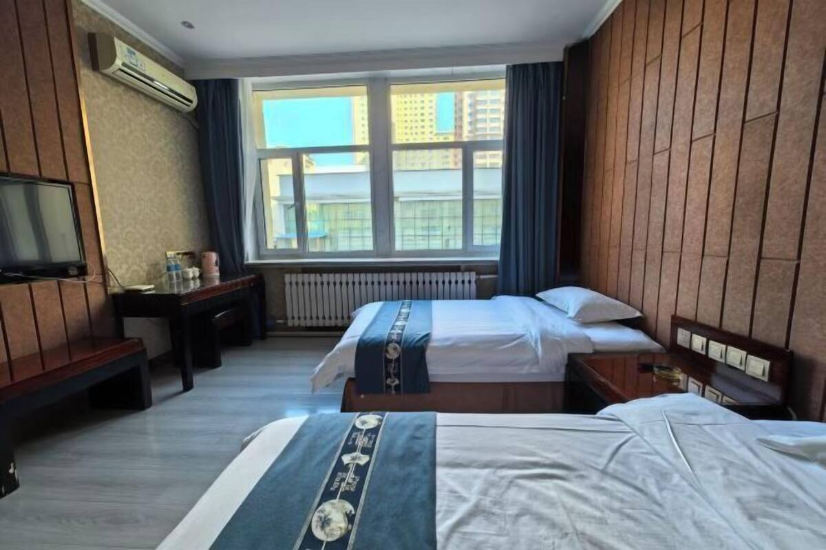 Une chambre d’hôtel avec deux lits, une télévision, un bureau et une fenêtre donnant sur des immeubles.