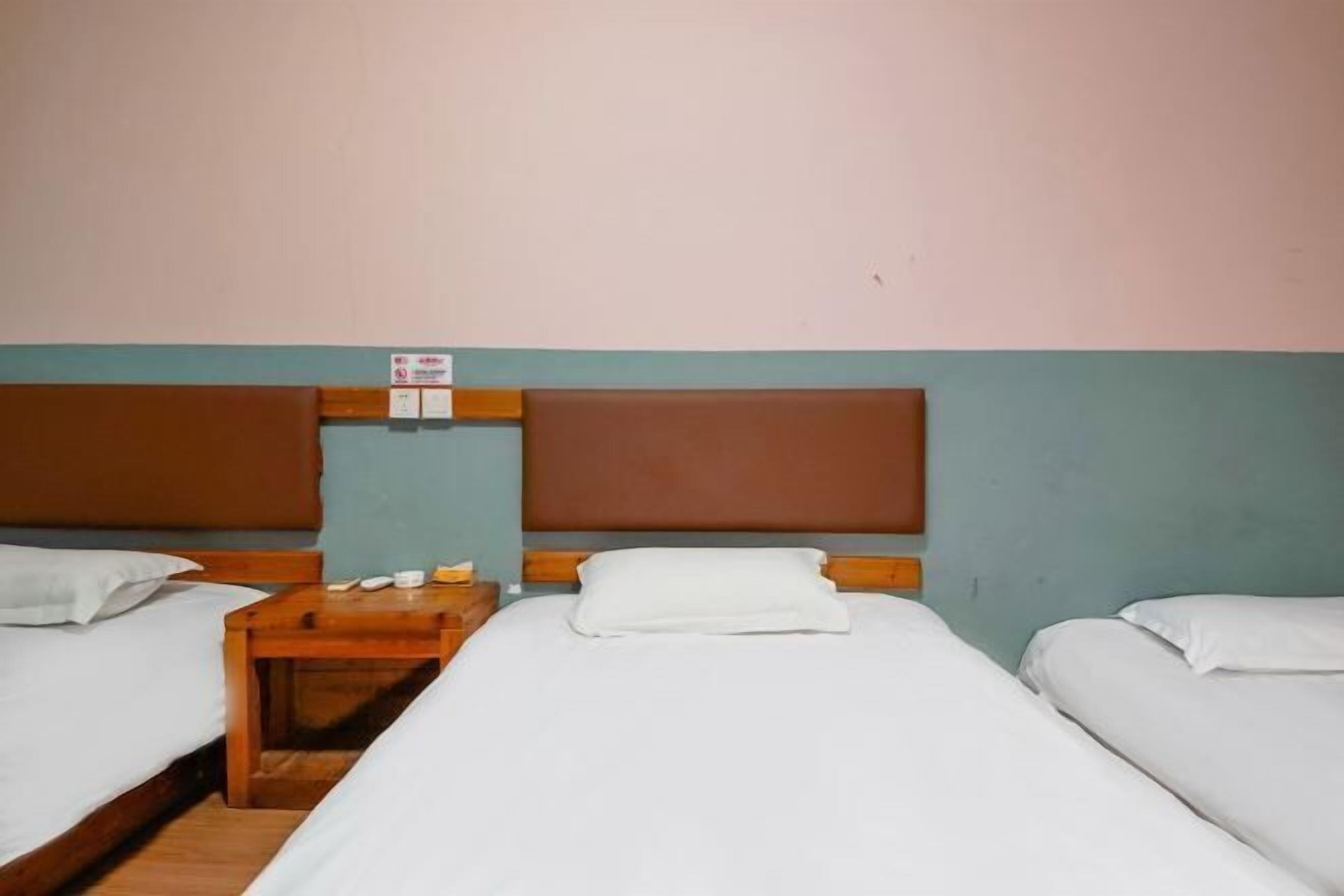 Una habitación de hotel con dos camas individuales, una mesita de noche de madera y un interruptor de luz en la pared.