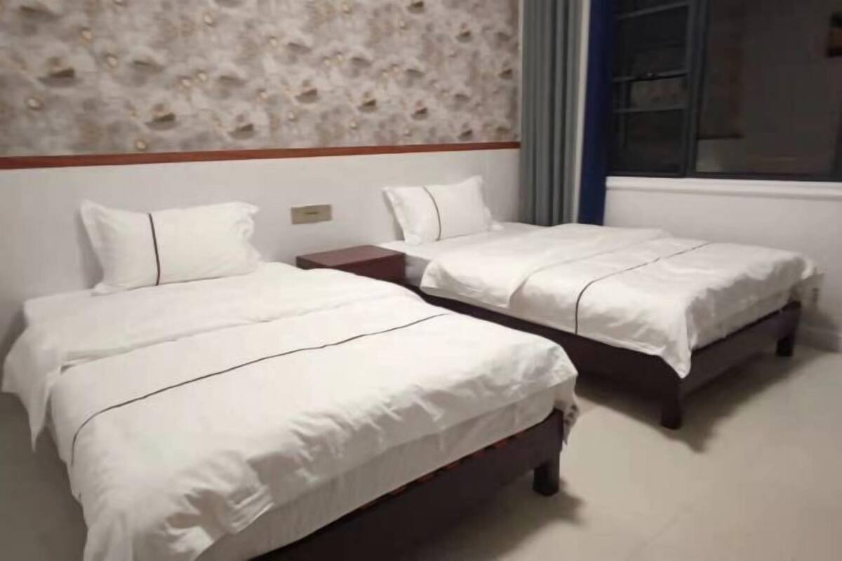 A hotel room with two single beds, a wooden headboard, a stone-patterned wall, and a window with curtains.