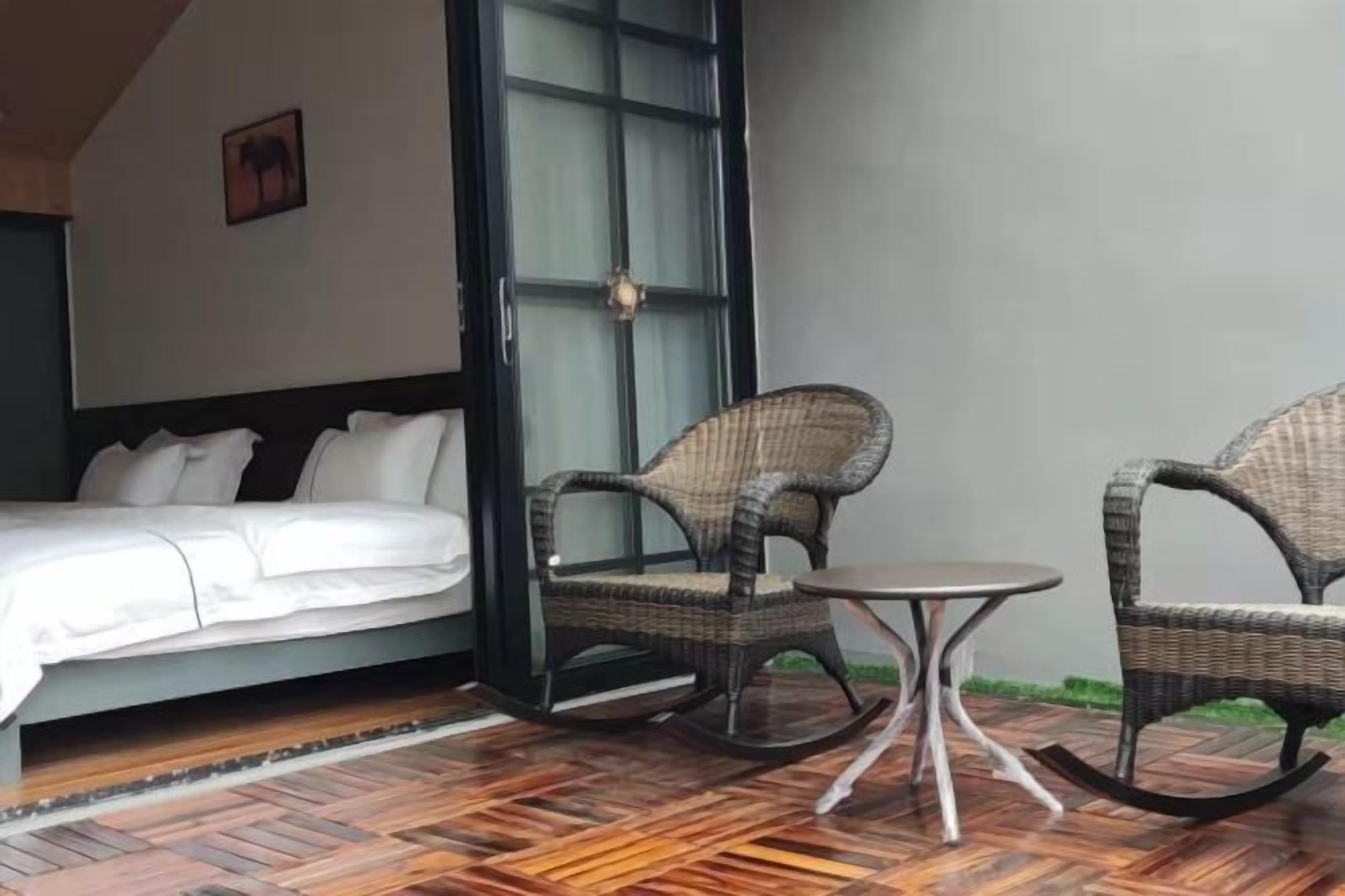 Een kamer met een bed, rieten schommelstoelen, een klein rond tafeltje en een groot raam.