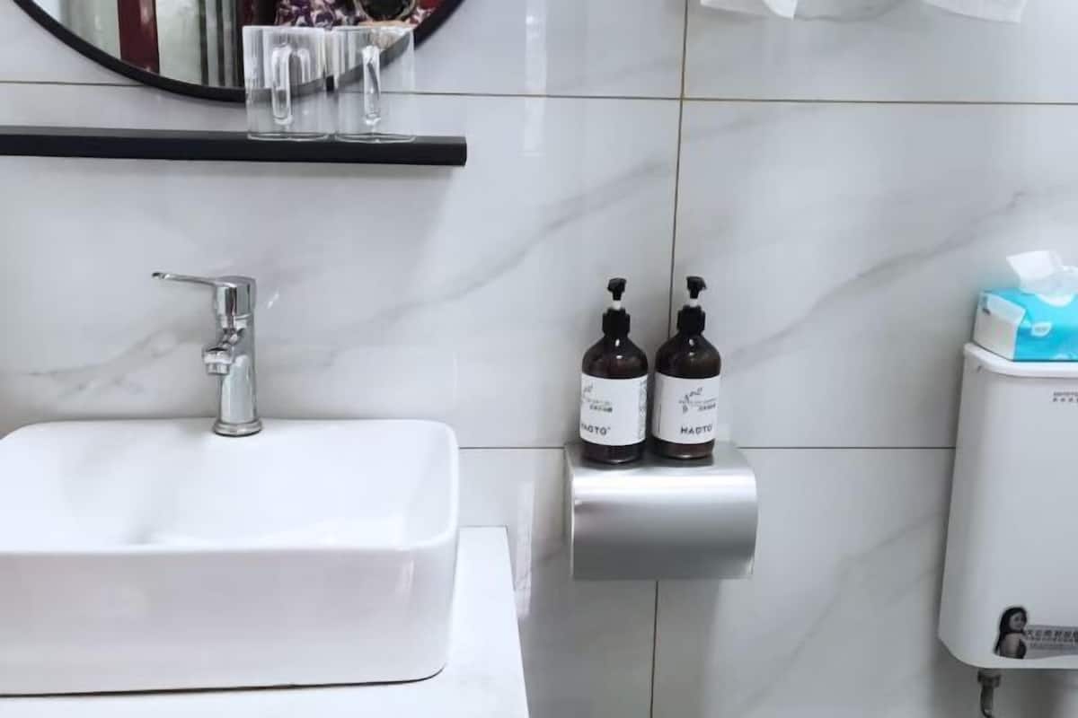 A bathroom with a white sink, a mirror, two soap dispensers, and a tissue dispenser.