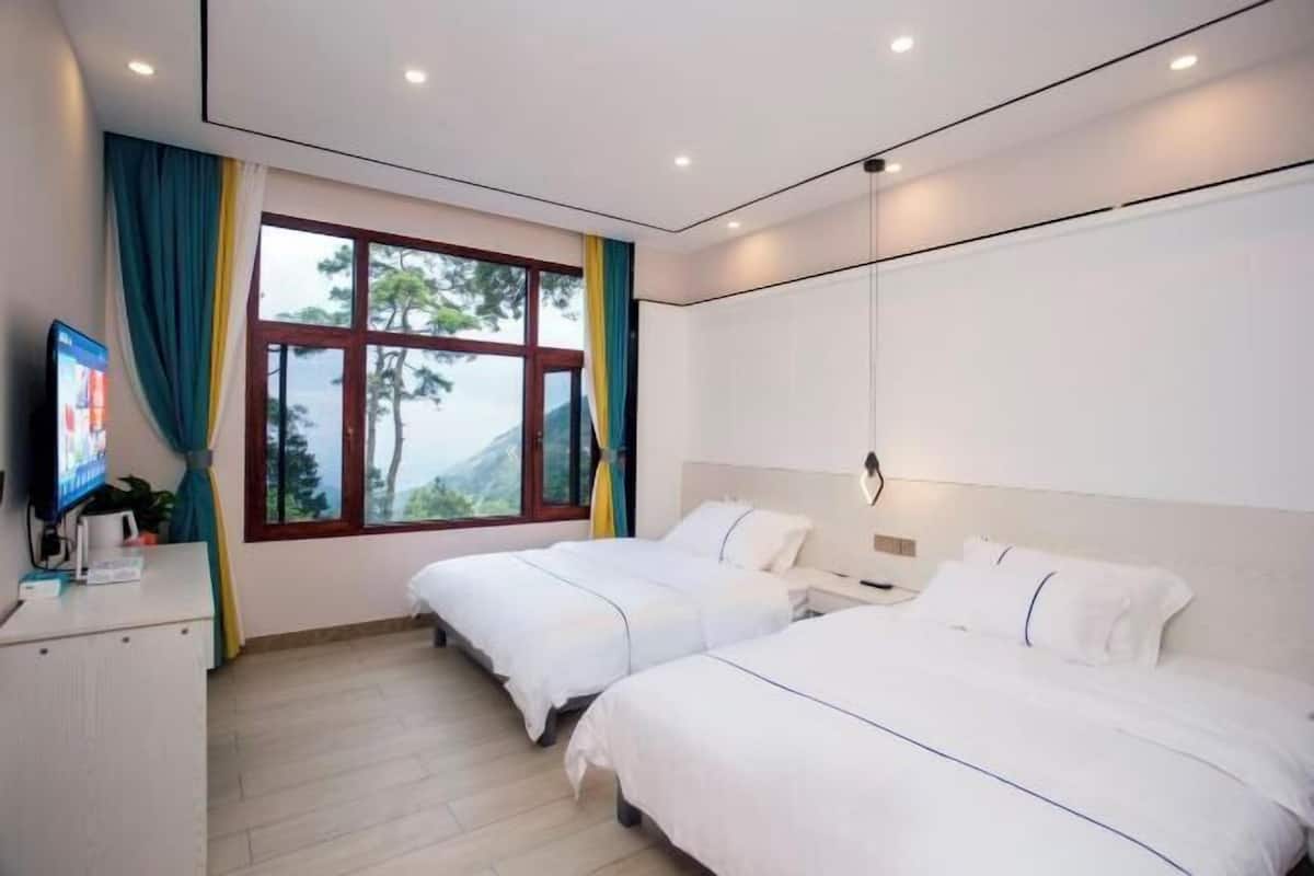 A hotel room with two beds, a desk, a TV, and a window with curtains.