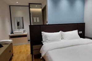 A modern hotel room with a large bed, a bedside table, a built-in sink, and a mirror.