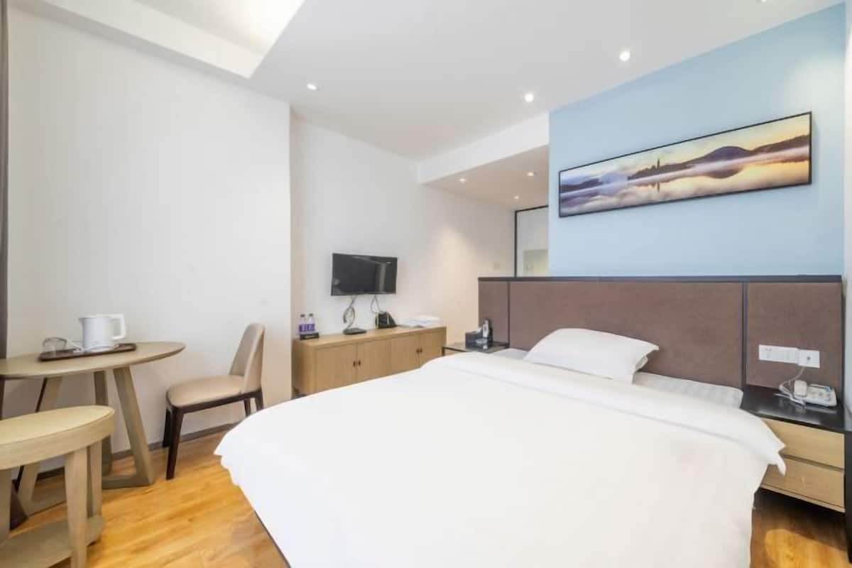 A hotel room with a bed, a desk, a chair, a television, and a painting on the wall.
