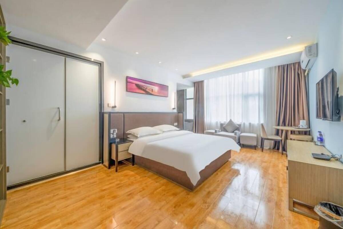 A modern hotel room with a large bed, a desk, a chair, and a TV.