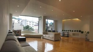 A spacious living area with a large sofa, a small table, and a view of the city through large windows. - Hotels in Bama (Bama)