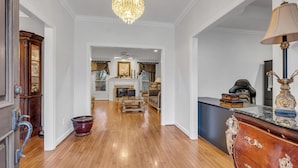 Un vaste salon doté d’un parquet en bois, d’un lustre, d’une cheminée et d’une grande armoire en bois.