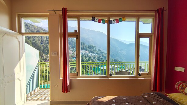 Une chambre dotée d’une grande fenêtre donnant sur les montagnes, d’un lit avec une couette à motifs et d’un balcon avec une balustrade.