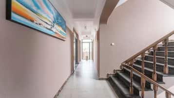 A hallway with a staircase, a painting on the wall, and a door at the end.