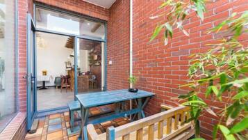 Un patio con una mesa, un banco, un muro de ladrillo y una puerta que da a un espacio interior.