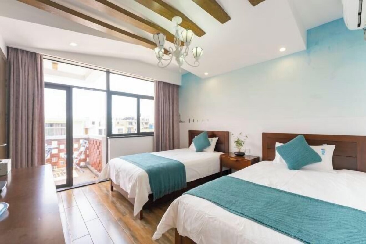 A hotel room with two beds, a large window, a chandelier, and a balcony view.