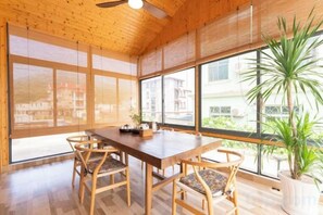 A wooden interior with a dining table and chairs, large windows, and a potted plant.