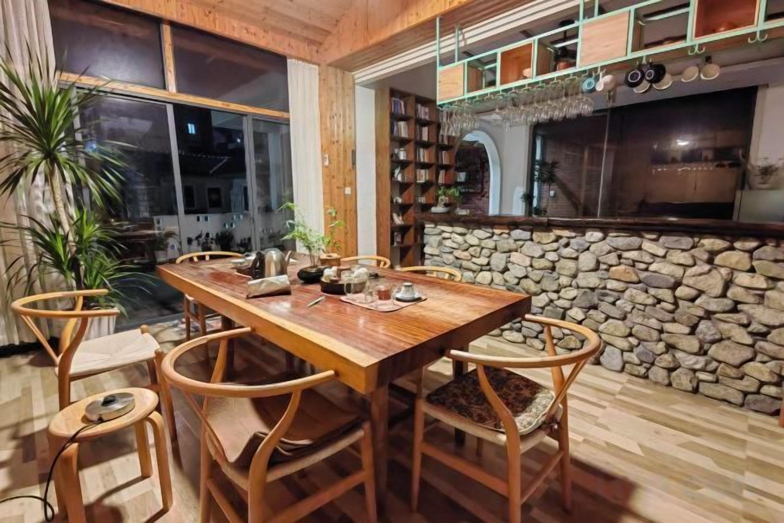 A dining area with a wooden table and chairs, a stone wall, and a kitchen area with a stone oven.