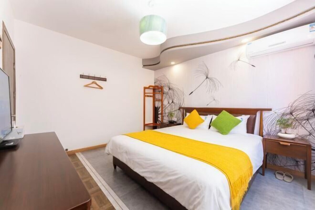 A bedroom with a bed, bedside tables, a desk, and a hanging plant.