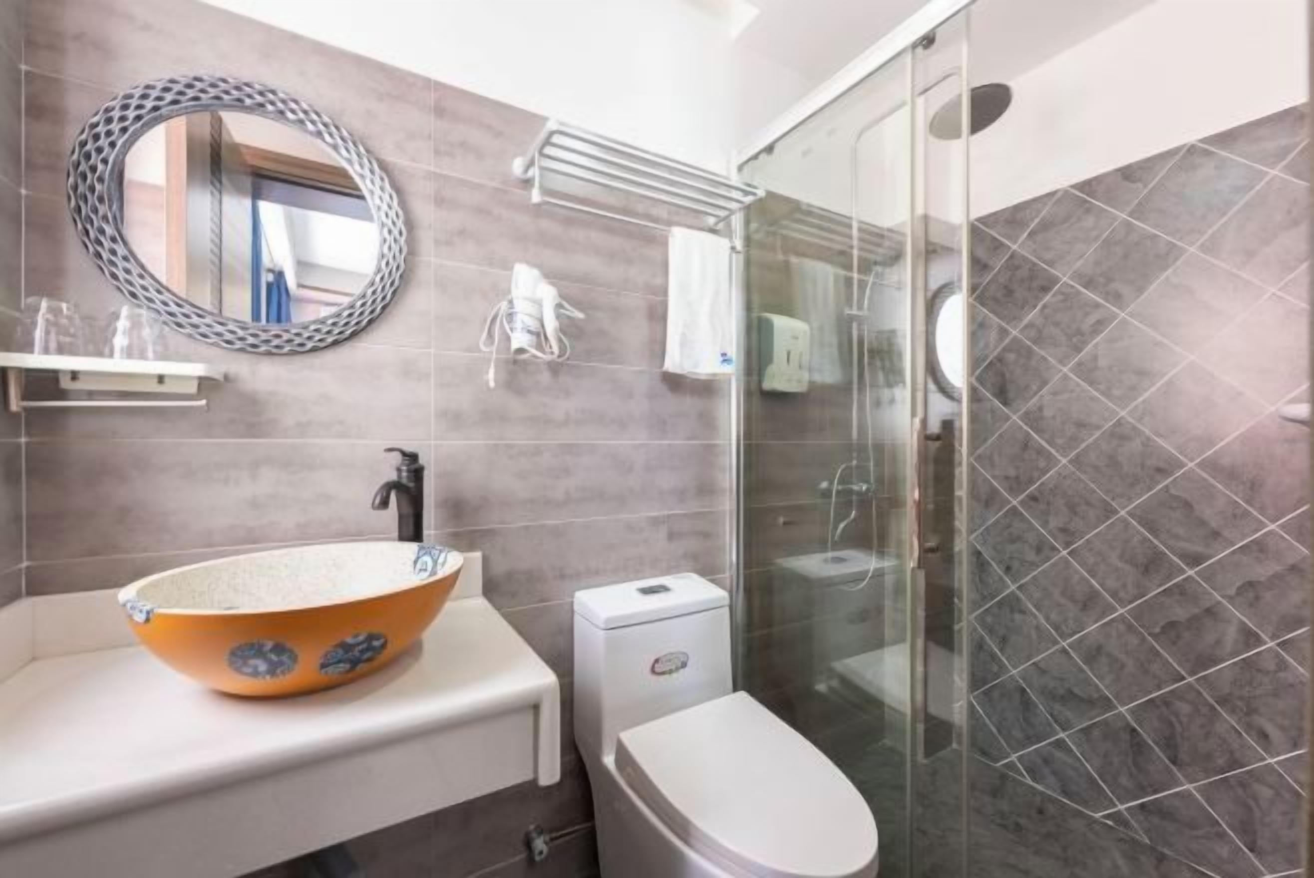 A modern bathroom with a round mirror, a vessel sink, a toilet, and a glass-enclosed shower.
