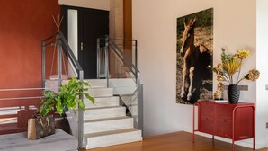 A staircase with a glass railing, a red metal console table with a vase, and a large framed picture on the wall. - Amazing 4 bedroom Villa with sea view pool (Alella Parc)