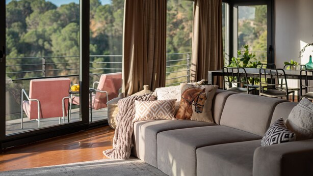 A modern living room with a large sofa, a horse statue, and a dining area with a view of the forest. - Amazing 4 bedroom Villa with sea view pool (Alella Parc)