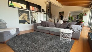 A modern living room with a grey sectional sofa, a grey shag rug, wooden flooring, and a wooden ceiling. - Amazing 4 bedroom Villa with sea view pool (Alella Parc)