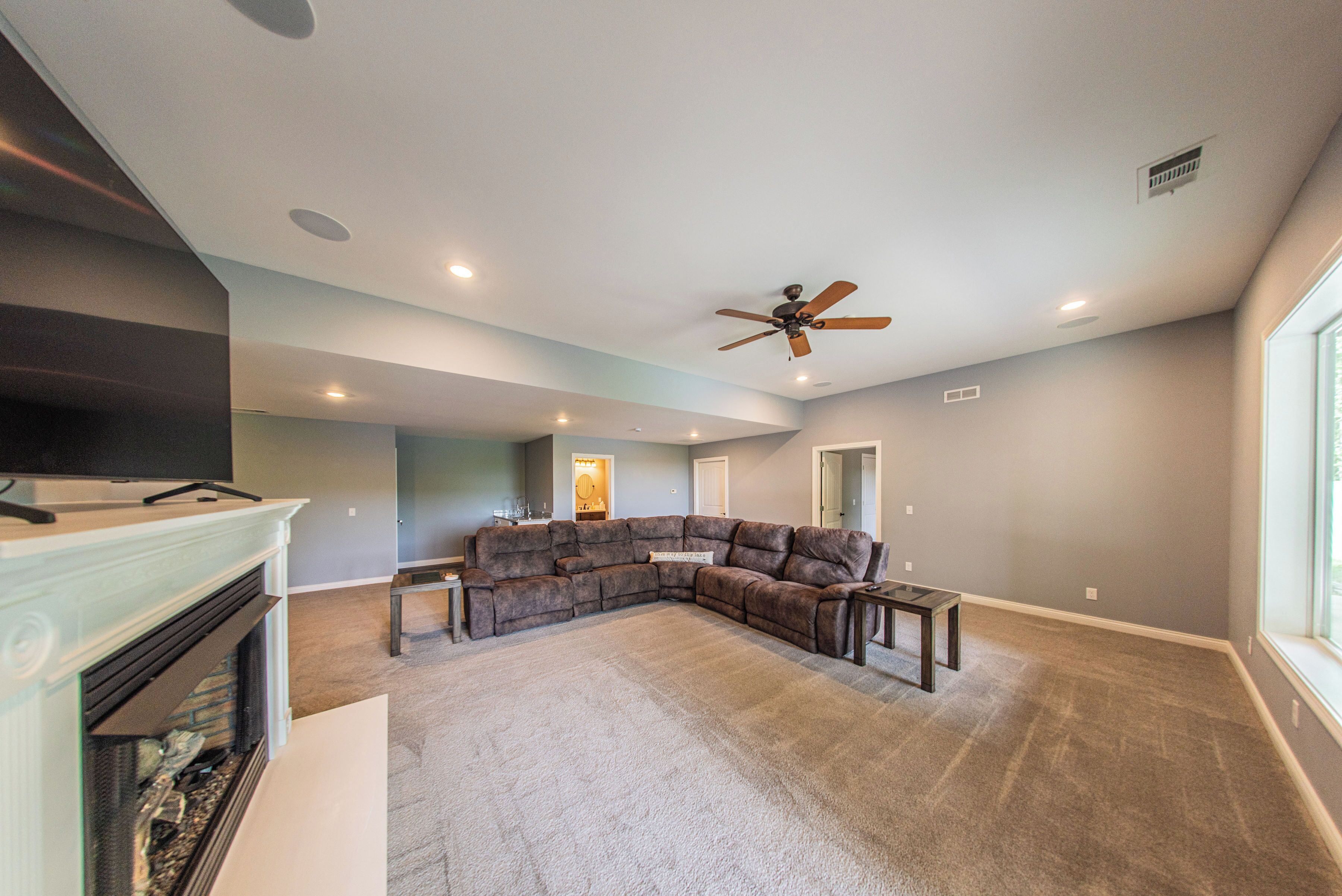 A spacious living room with a sectional sofa, a fireplace, a ceiling fan, and recessed lighting.