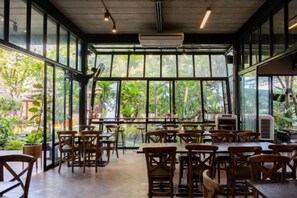 An indoor dining area with tables and chairs, large windows, and a view of greenery outside. - Crystal Resort (Nakhon Ratchasima)