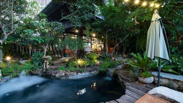 A serene garden with a pond, wooden deck, and an umbrella. - Crystal Resort (Nakhon Ratchasima)